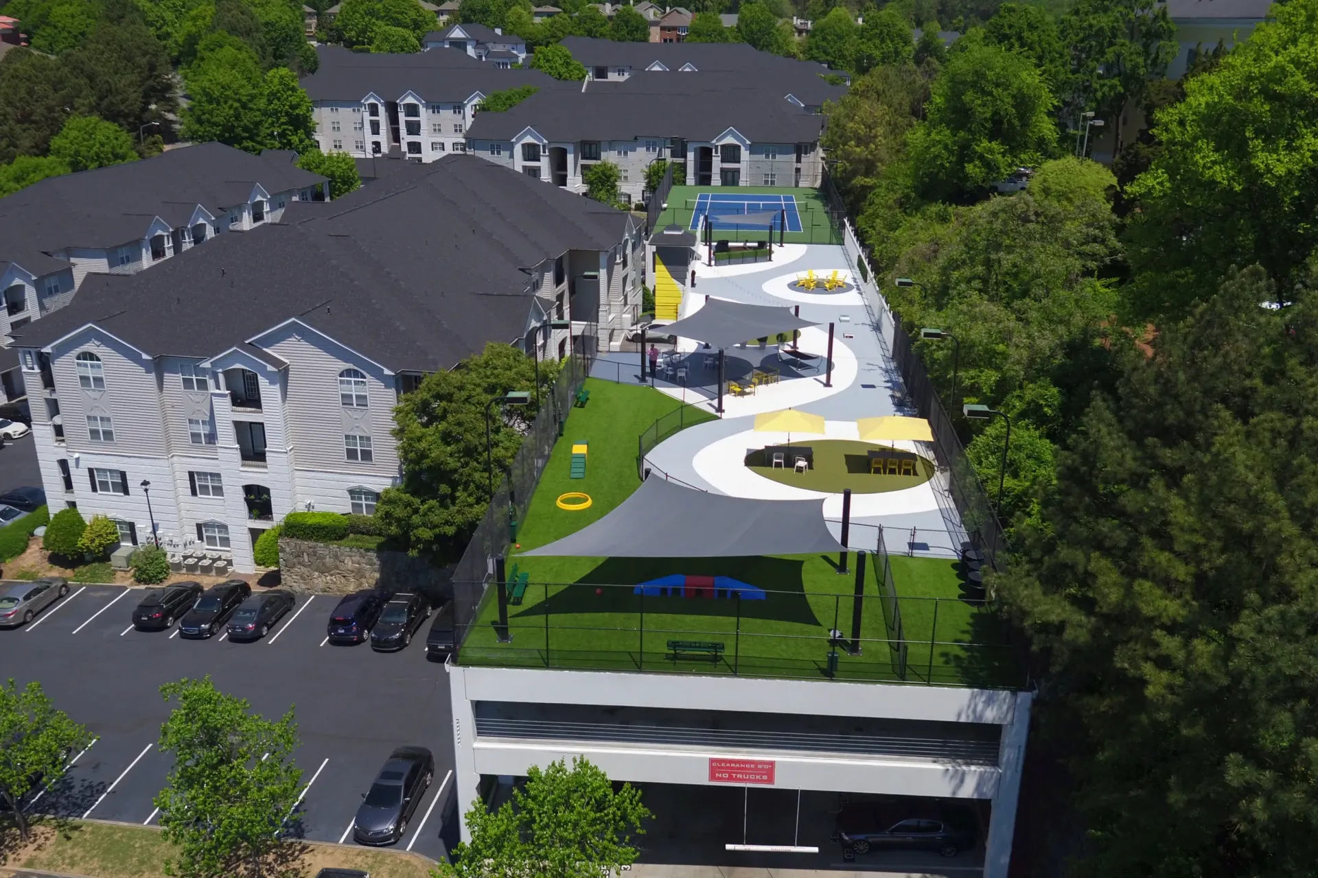 Aerial view of a rooftop amenities deck with a tennis court, lounge areas, and a dog park.