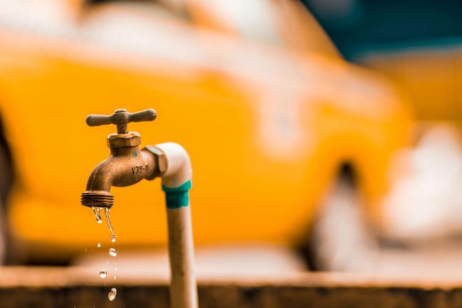 Dripping faucet with water drops, in front of a blurred yellow car.