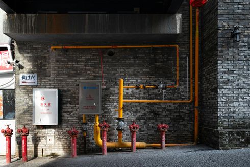 Brick wall with red fire hydrants, yellow gas pipes, and a white cabinet.