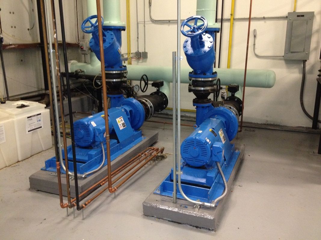Two blue industrial pumps with valves and pipes in a mechanical room.