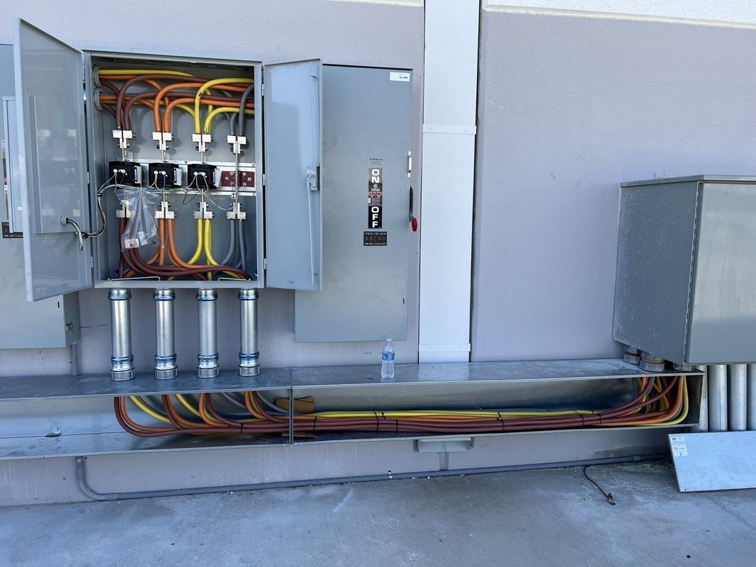 Electrical panel with open doors, revealing wires. Conduit runs along the base of the wall.