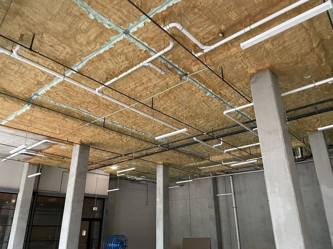 Interior view of a construction site with exposed pipes, insulation, and concrete pillars.