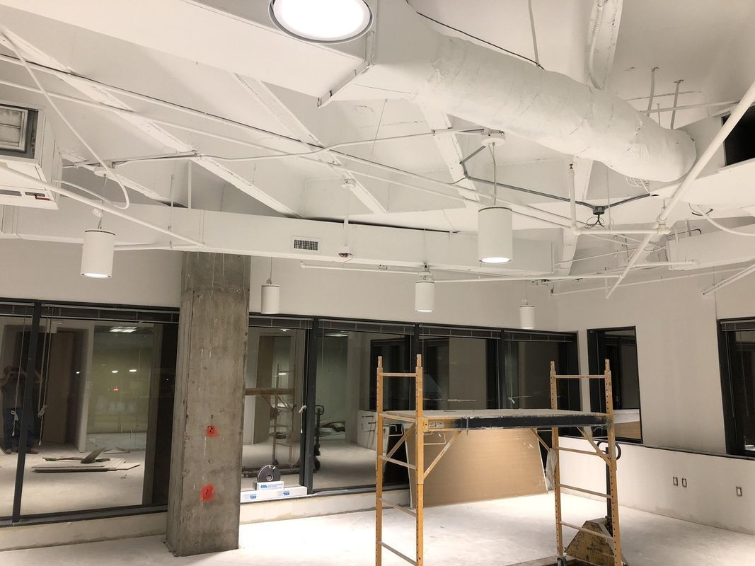 Interior of a building under construction, white walls, exposed ceiling ductwork, scaffolding, windows.