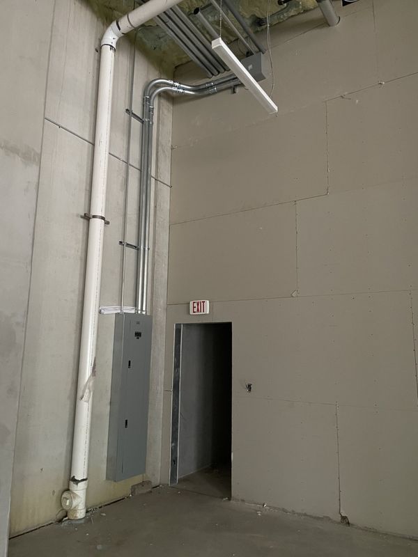 Electrical conduit and a panel on a wall near a doorway with an exit sign.