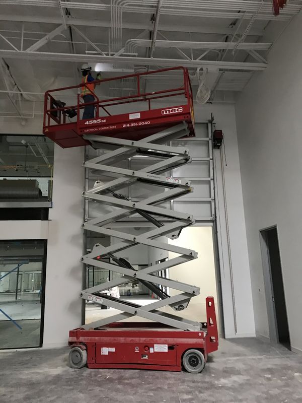 A person on a red scissor lift working on a ceiling inside a construction area.