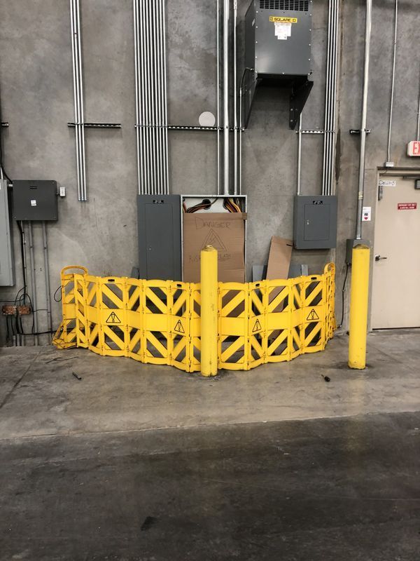 Yellow safety barrier around equipment against a concrete wall.