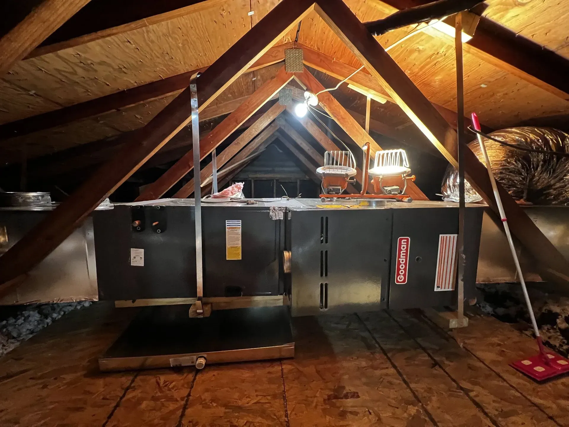 Attic HVAC unit under exposed wooden rafters, lit by a hanging bulb.