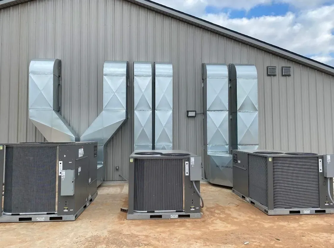 Outdoor HVAC units in front of a metal industrial building with large duct vents.