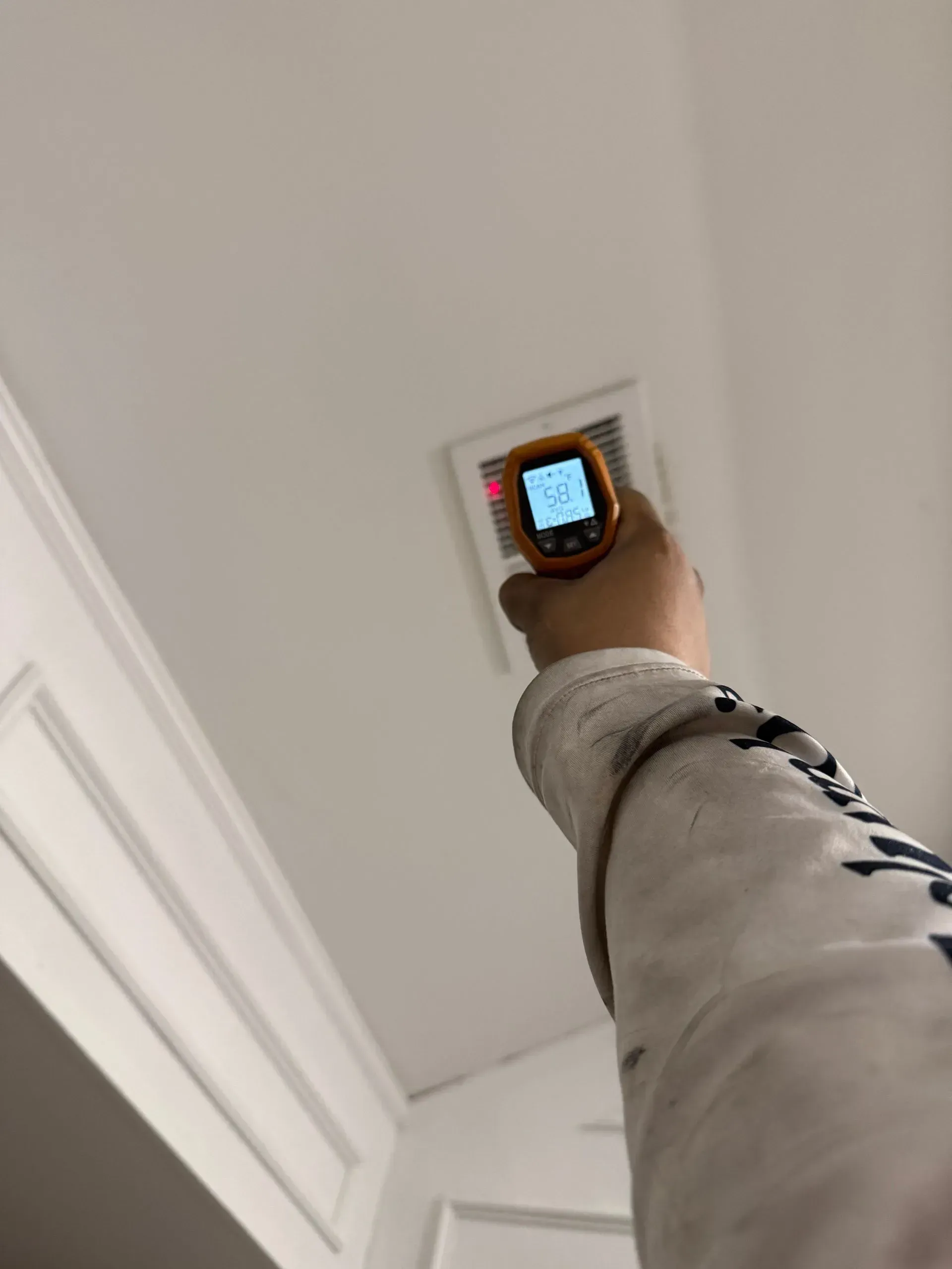 Hand holding a smartphone up to a ceiling-mounted smoke detector in a white room