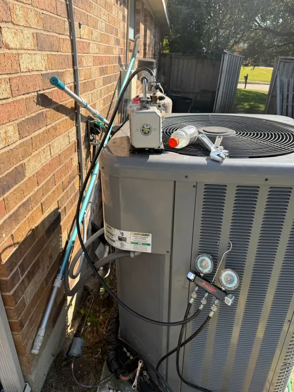Outdoor air conditioner unit beside a brick wall with service gauges and hoses attached