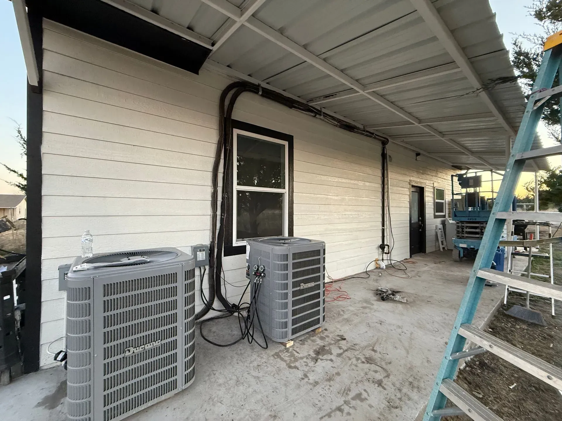 Exterior wall with two HVAC units, a door, and a blue ladder under a covered overhang