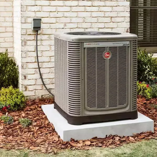 Outdoor central air conditioner unit on a concrete pad beside a brick house wall