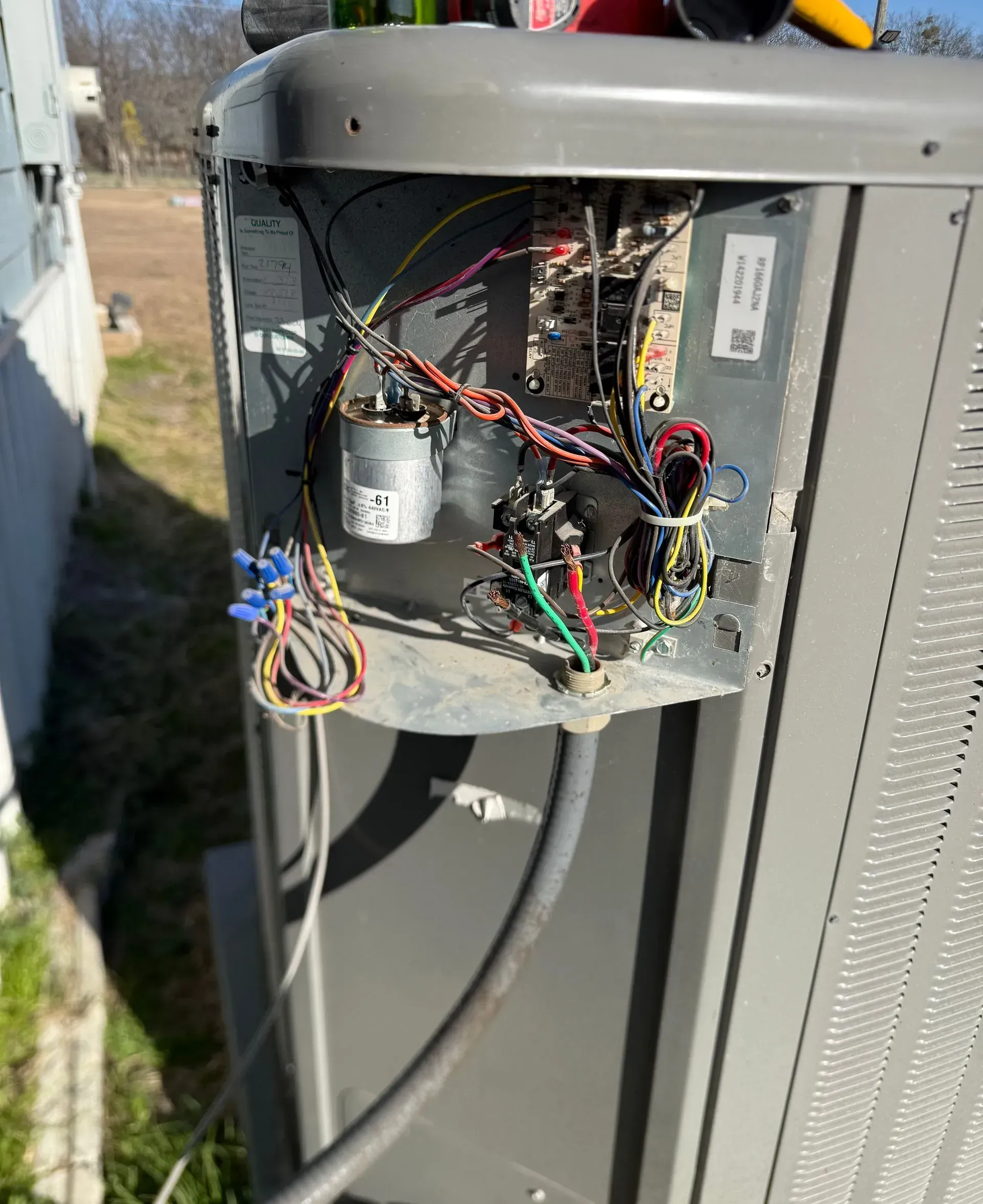 Open electrical panel with exposed wires and components on the side of an outdoor unit