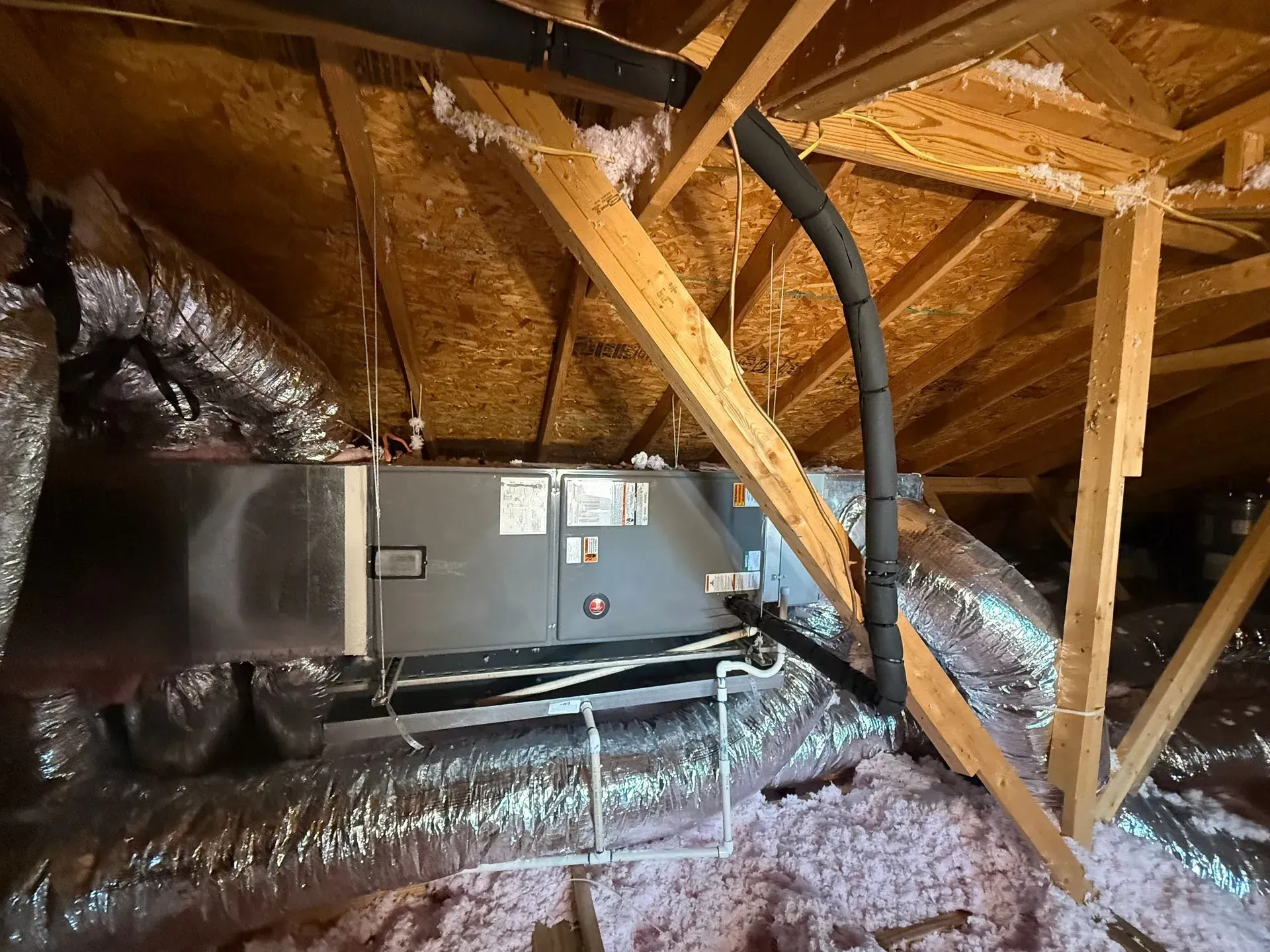 Attic with HVAC unit, ductwork, and wooden rafters wrapped in insulation