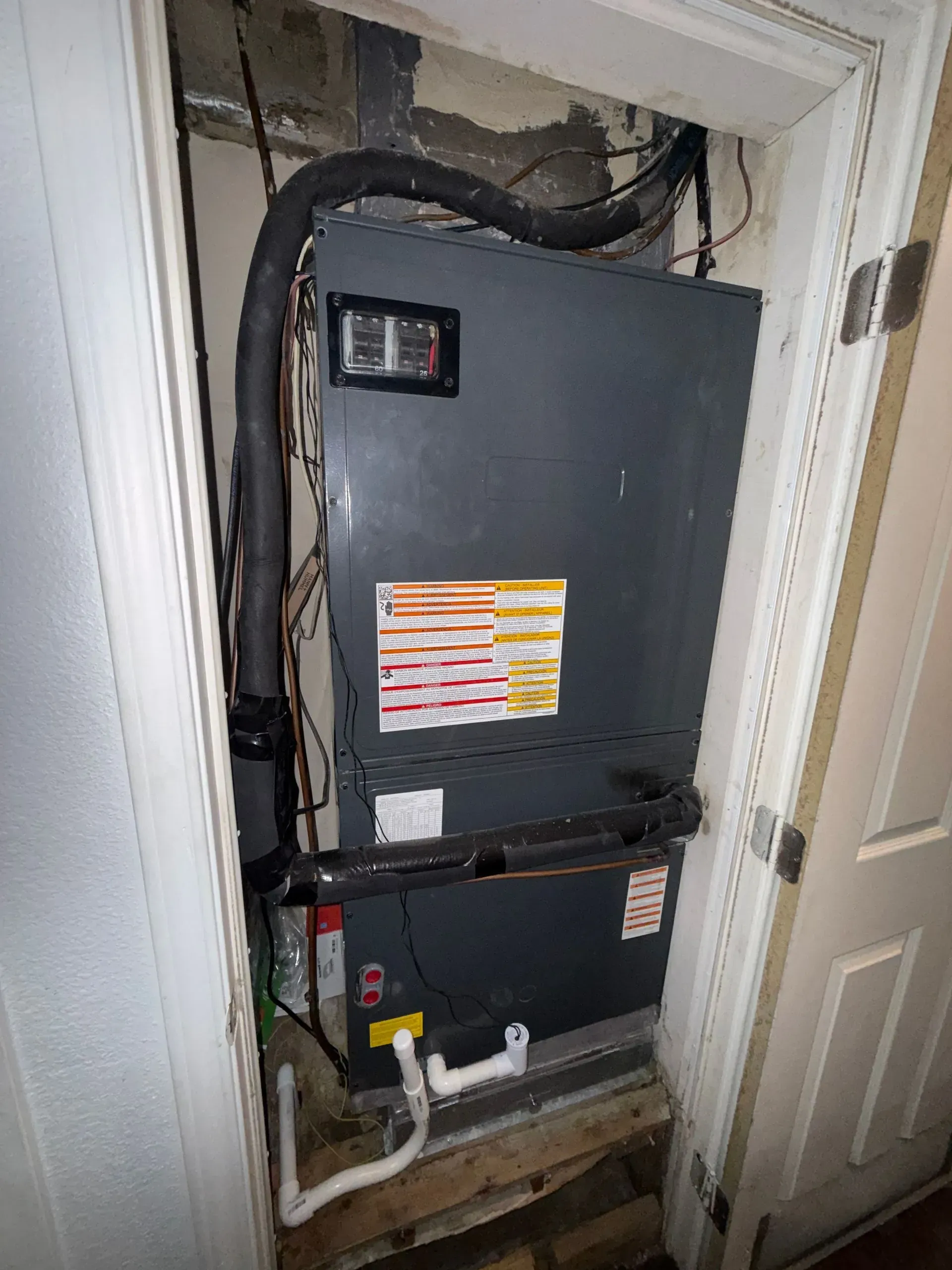 Open electrical panel in a closet with exposed wiring and ductwork above.
