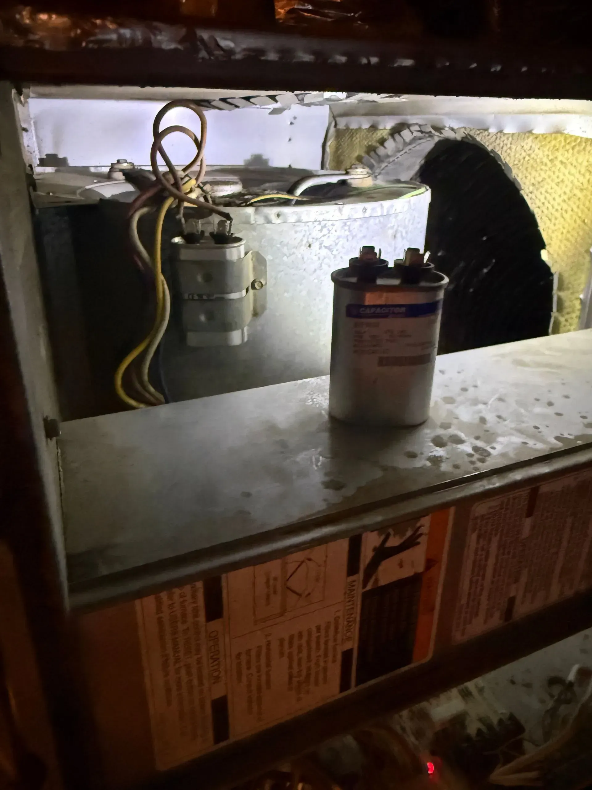 Messy under-sink area with pipes, wiring, and a small cylindrical container on a shelf