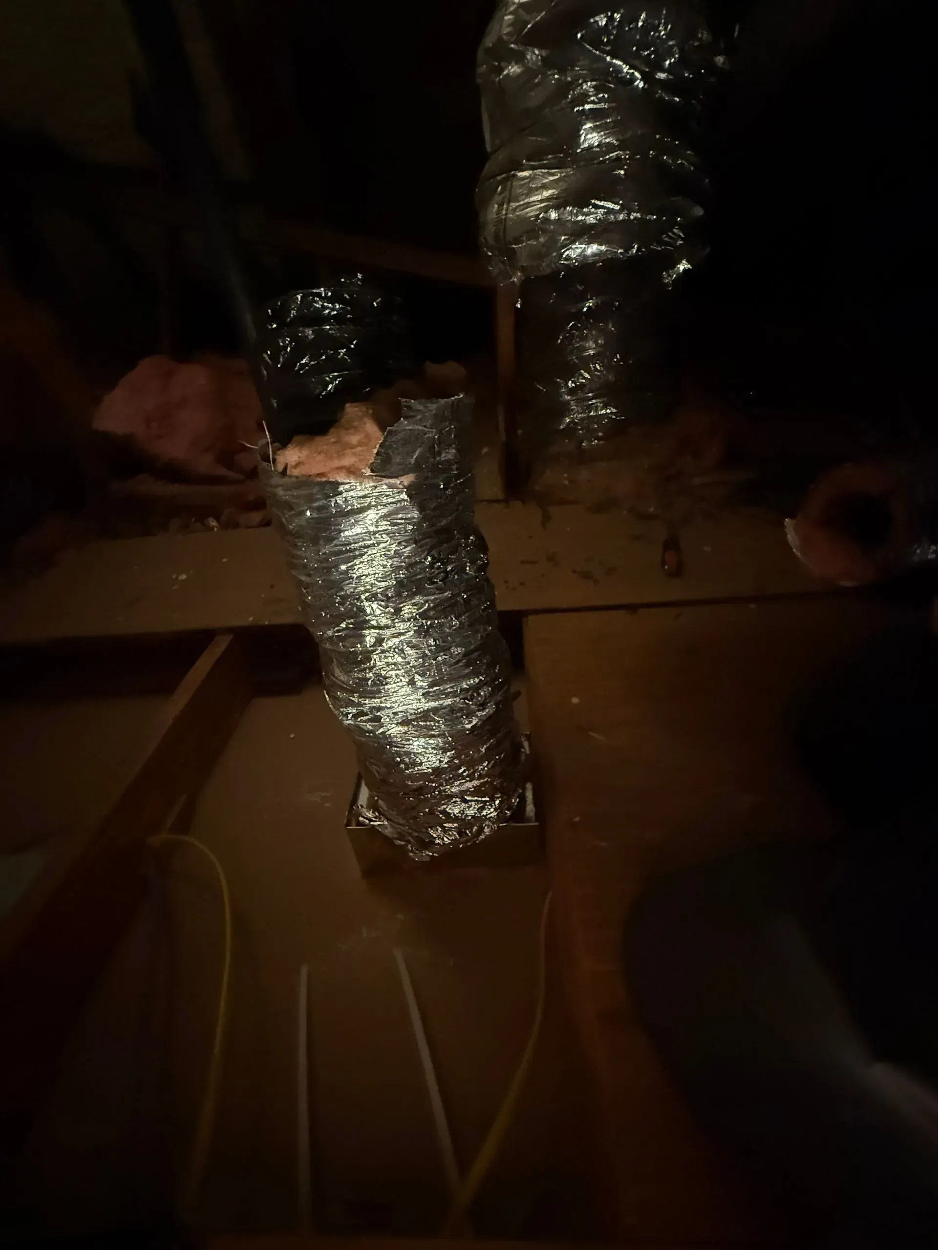 Foil-wrapped ventilation ducts in a dimly lit attic or crawlspace, with cardboard boxes below.