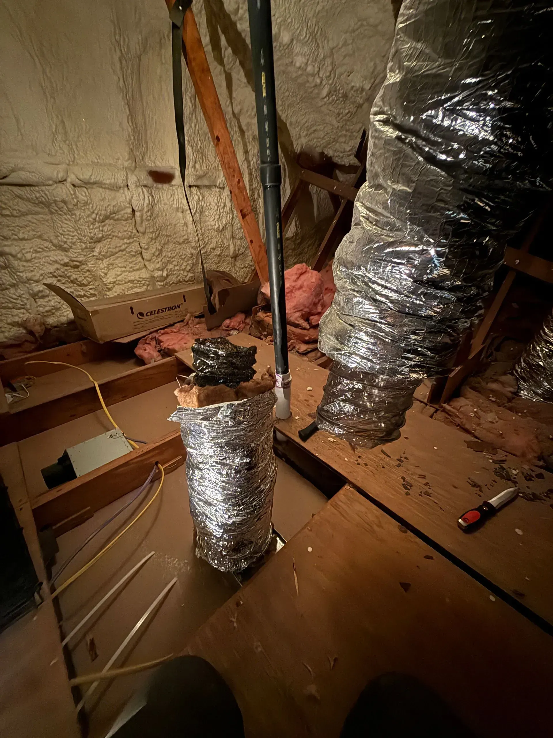 Foil-wrapped HVAC ducts and tools in an unfinished attic crawlspace with insulation and exposed framing