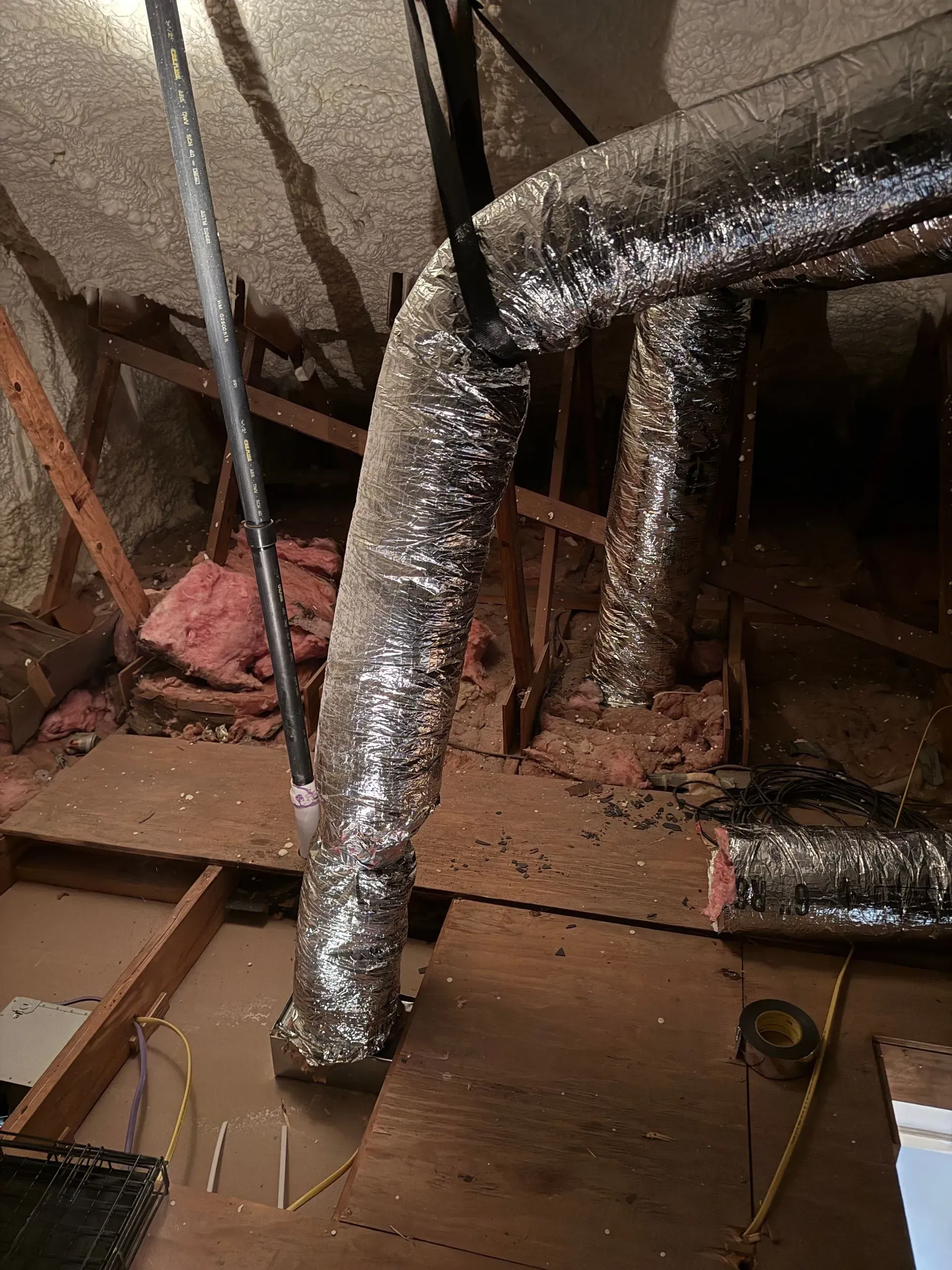 Foil-wrapped HVAC ducts in a dusty attic crawlspace with exposed framing and insulation.