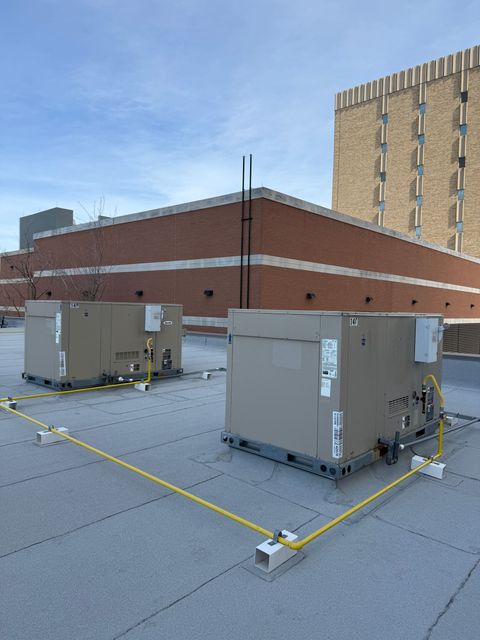 Rooftop HVAC units on a flat commercial roof beside a brick building and tall hotel tower