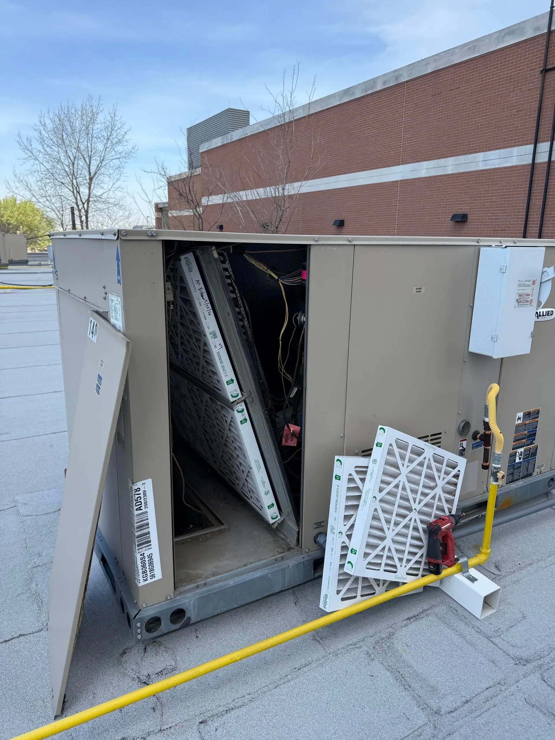 Damaged outdoor HVAC unit with bent panels and debris beside a brick building.