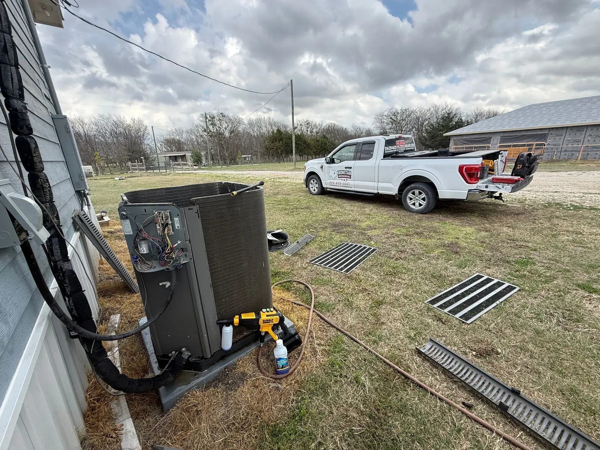 Outdoor HVAC unit beside a house with a white pickup truck parked in a grassy yard