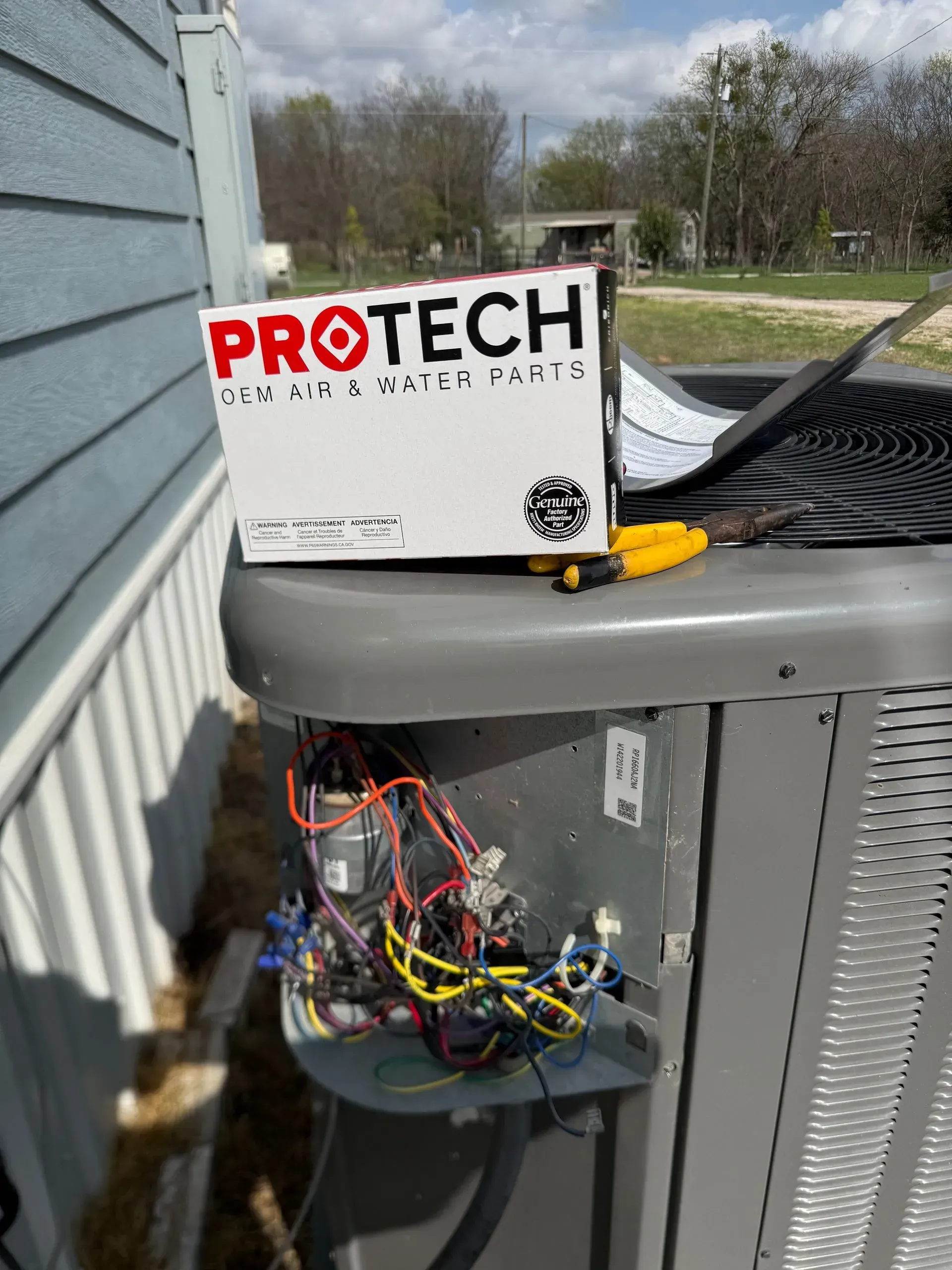 Open HVAC unit with exposed wiring and a PROTECH service label on top outdoors.