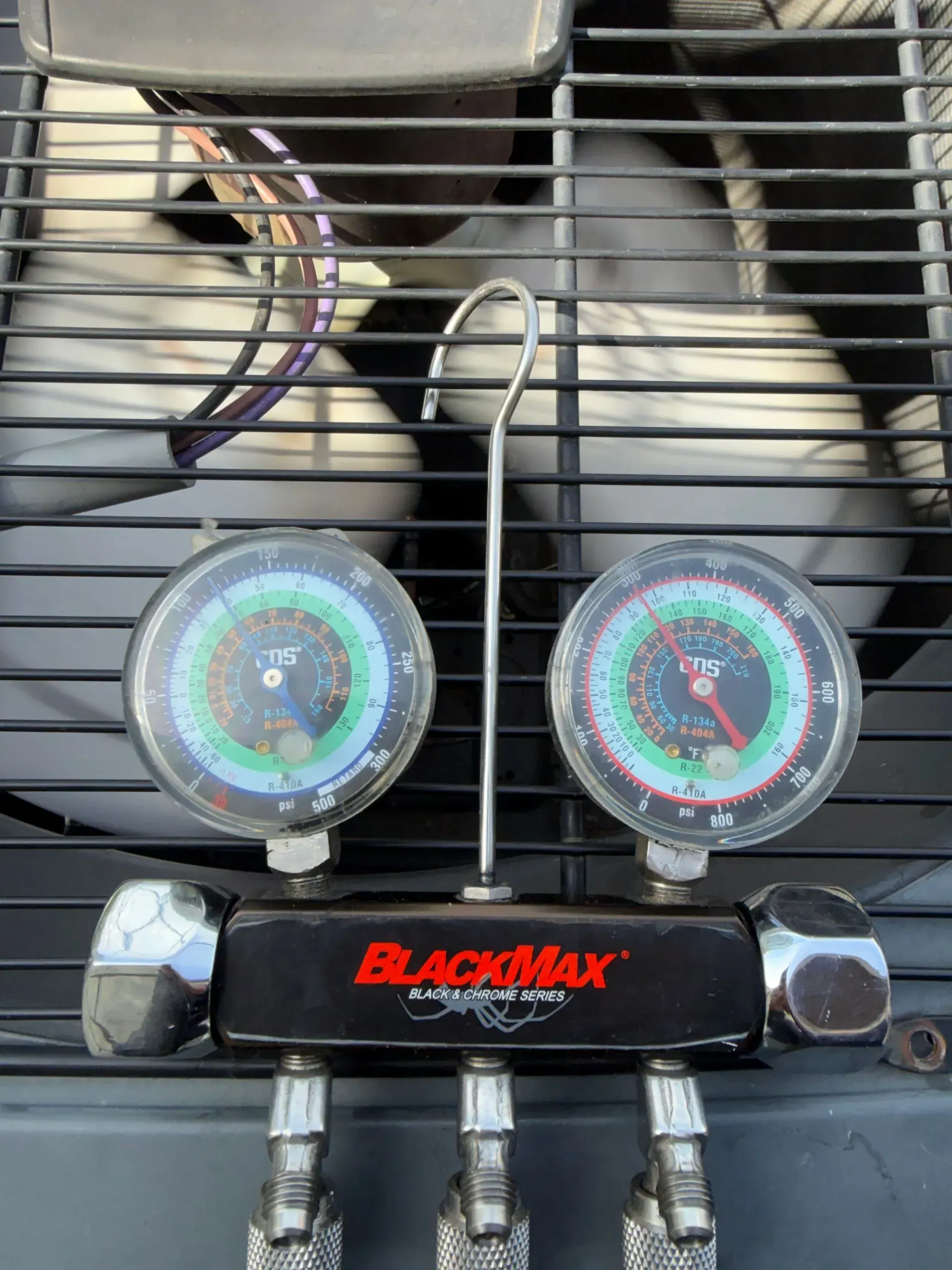 Dual gauges and fittings on a Blackmax manifold attached to an air conditioning unit.