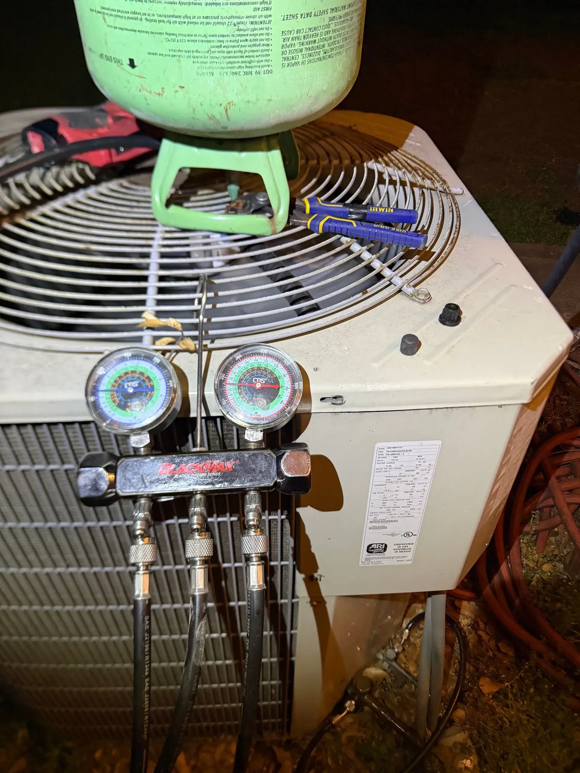 HVAC service gauges connected to an outdoor air conditioner unit with green tank on top