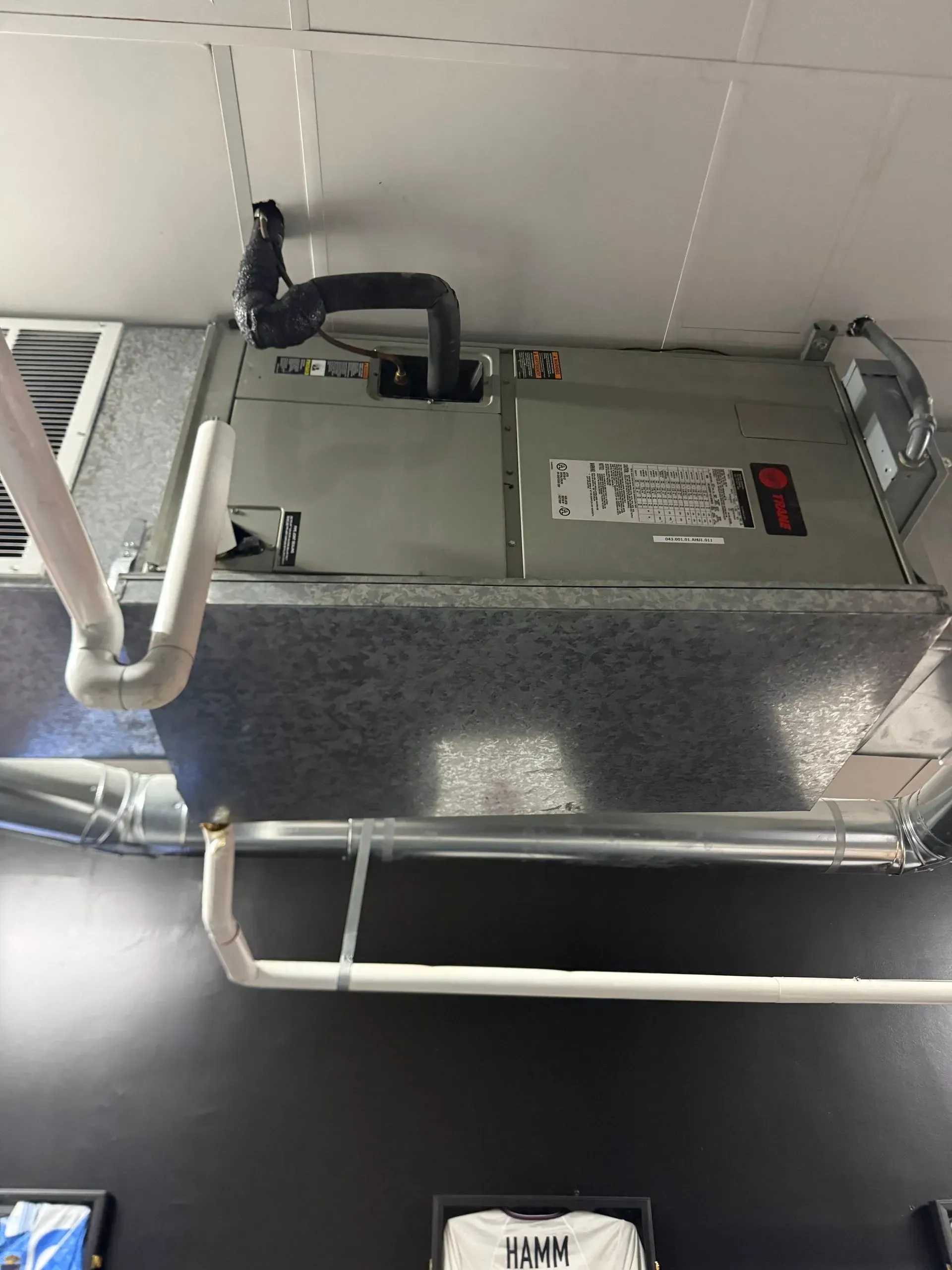 Ceiling-mounted HVAC unit with exposed ducts and white piping in an industrial interior