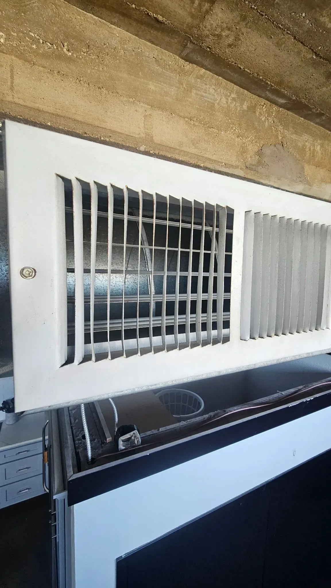 White barred vent or window cover mounted on a beige wall above a black appliance.