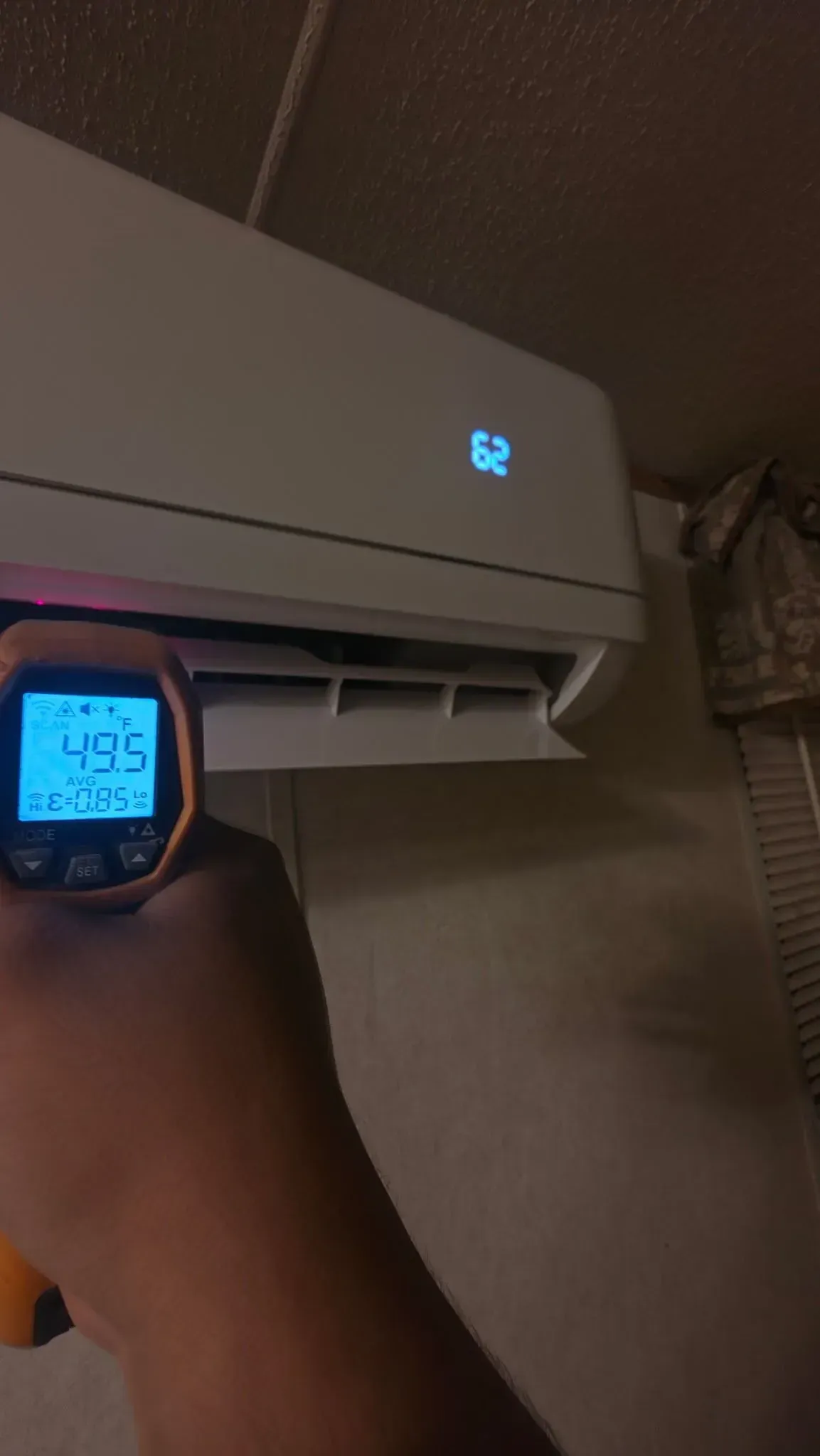 Digital thermometer held near a wall-mounted air conditioner, showing 42.5°F.