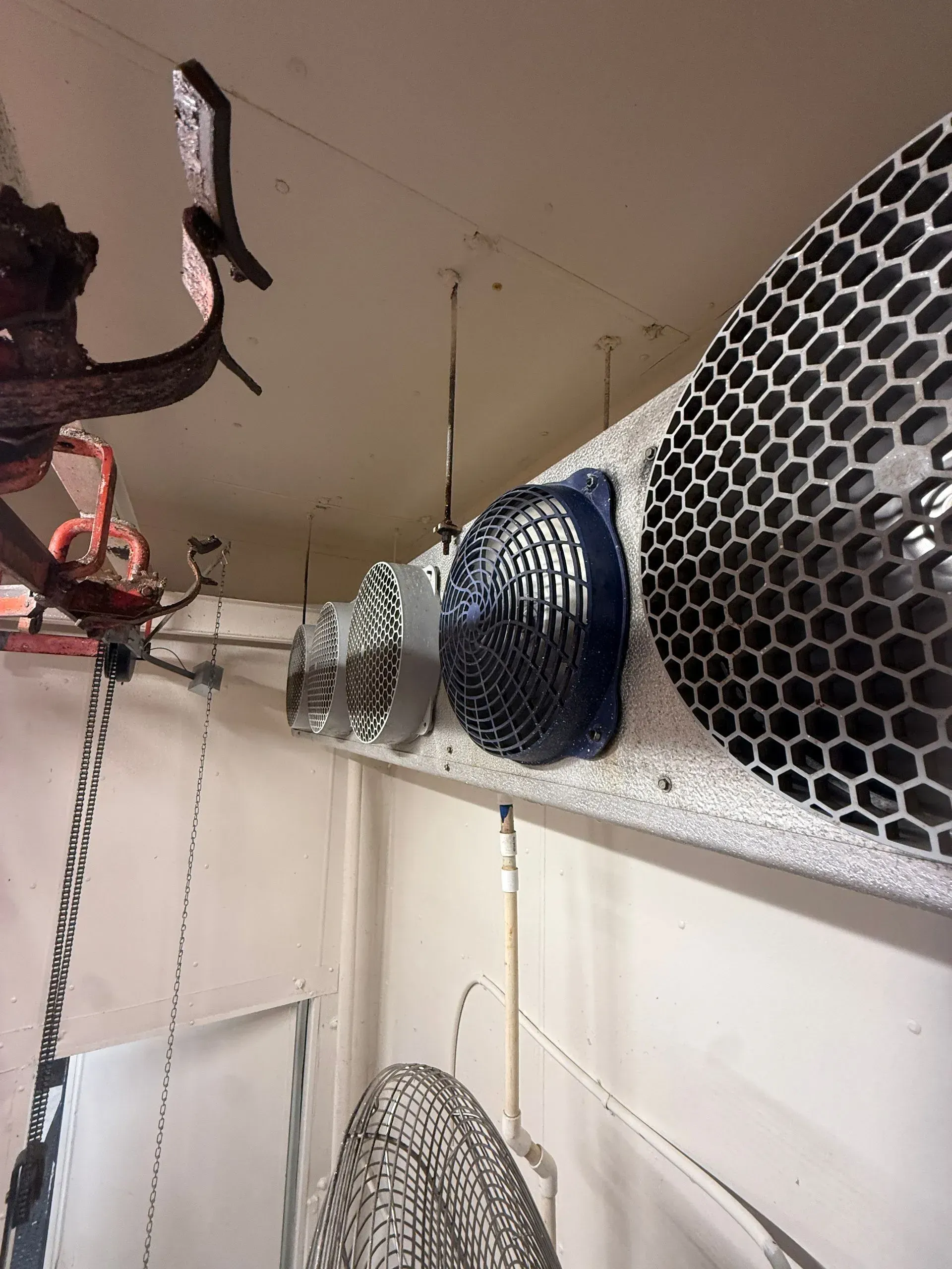 Ventilation ducts and fans mounted near a ceiling in an industrial or utility room