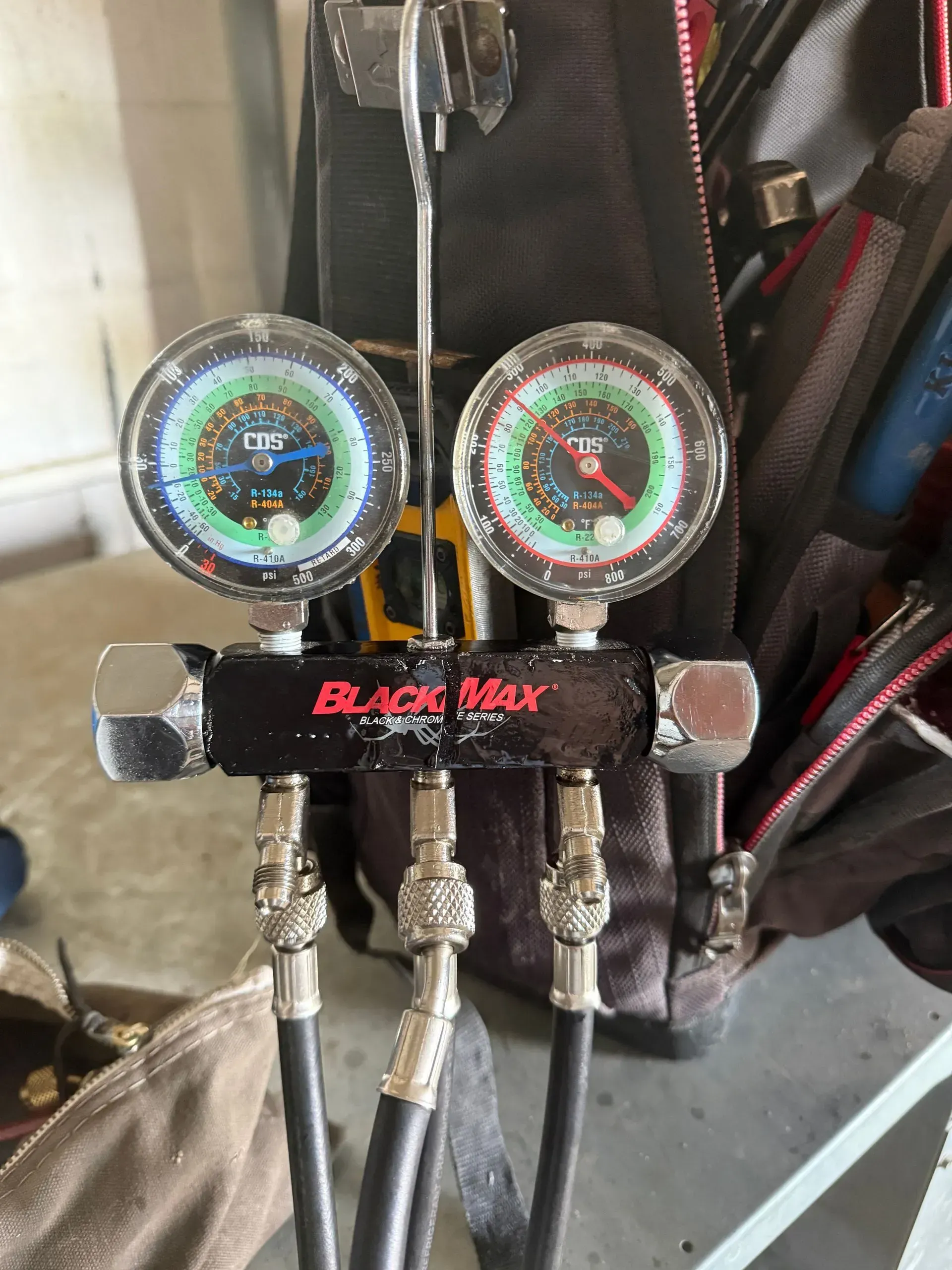 BLACK MAX dual gauge manifold with hoses attached to a backpack or tool bag in a garage setting