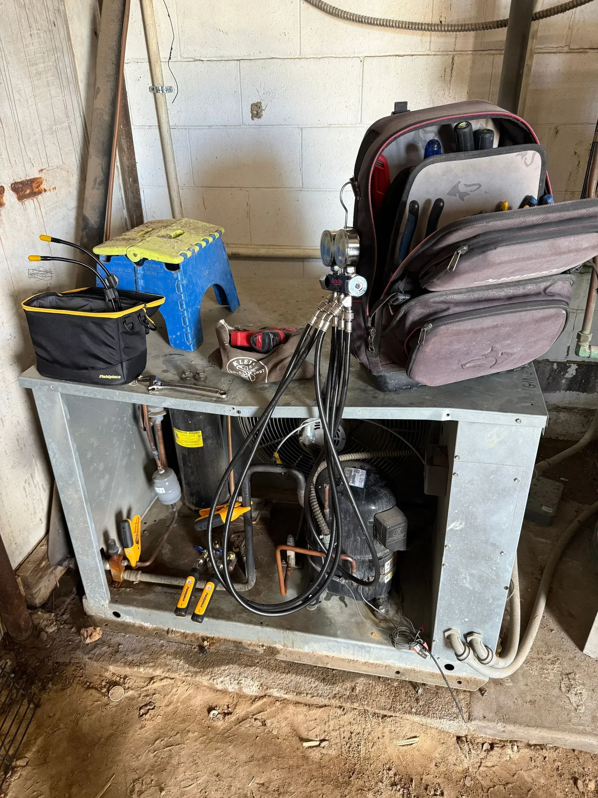 Two backpacks on a gray metal workbench in a concrete garage, with tools and cables below.
