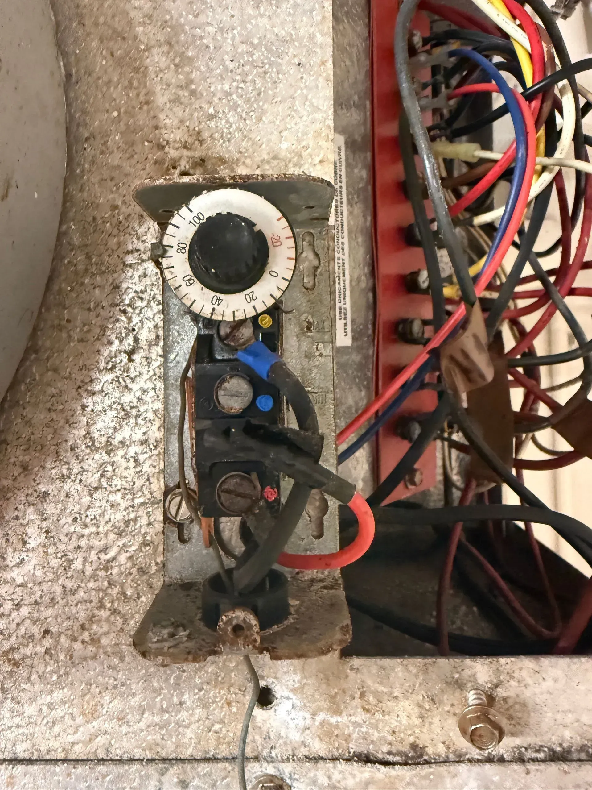 Close-up of a wall-mounted electrical component with wires, switches, and a red fuse block in a panel.