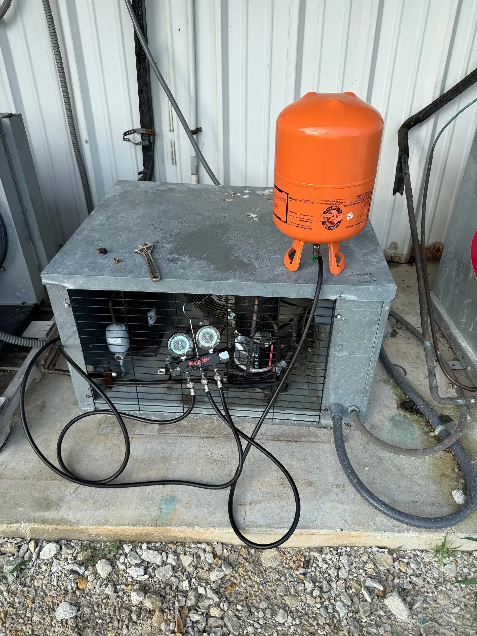 Industrial equipment with an orange tank on top, cables and gauges inside a metal enclosure outdoors