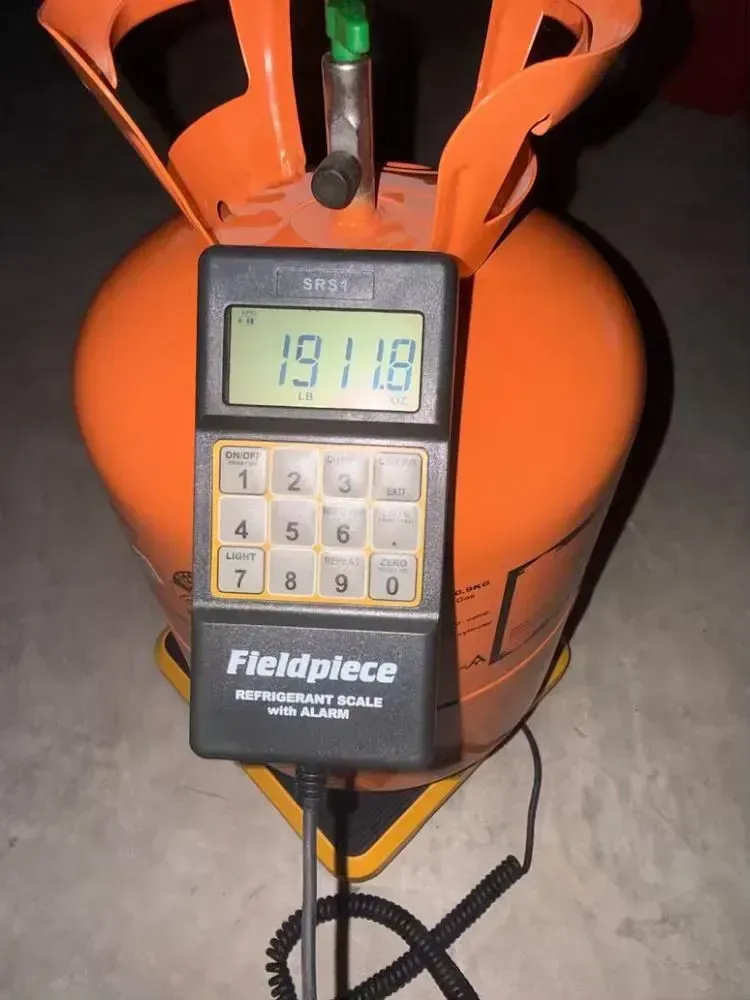 Digital hanging scale with keypad and display, suspended from an orange frame on a concrete floor.