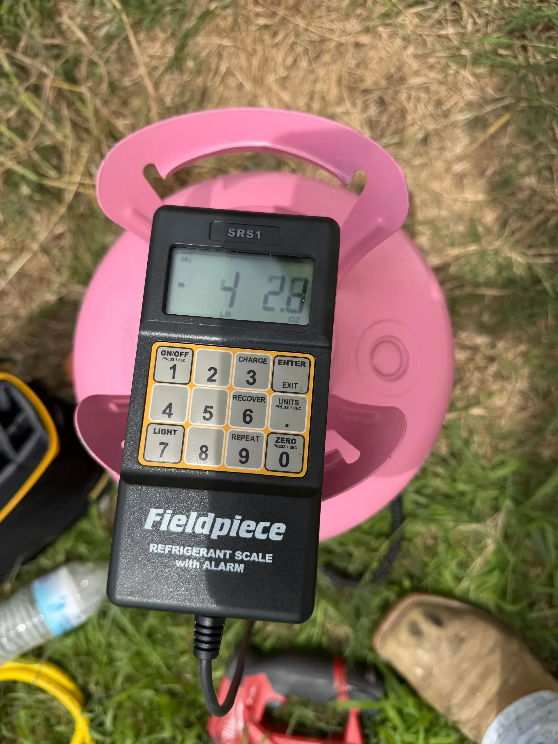 Handheld meter with keypad resting on a pink plastic seat outdoors on dry grass