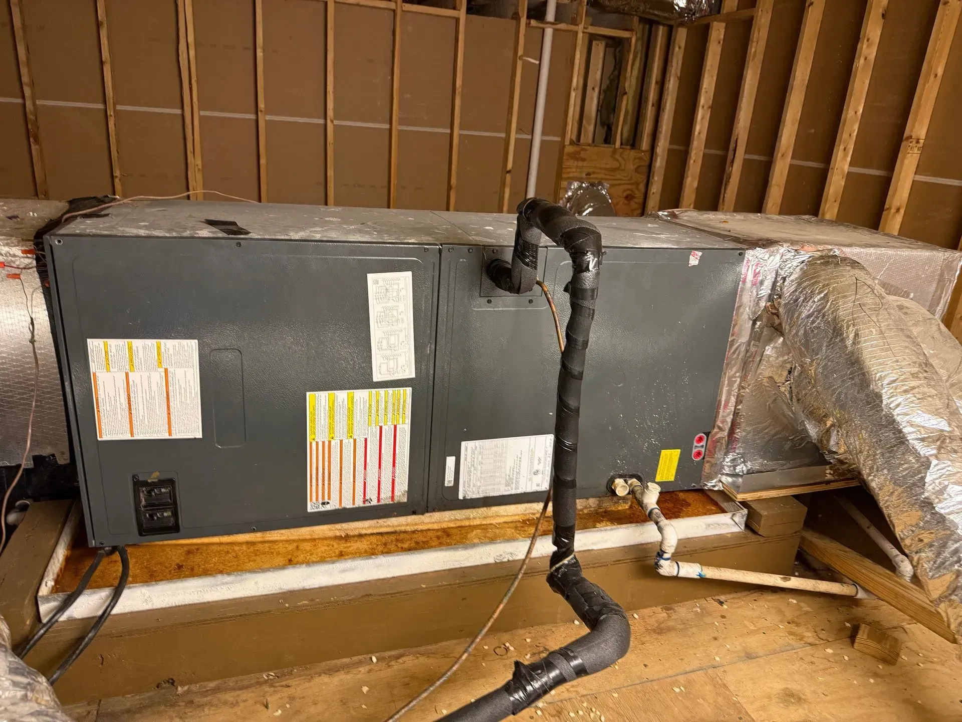 Attic HVAC air handler with insulated ductwork and exposed wooden framing