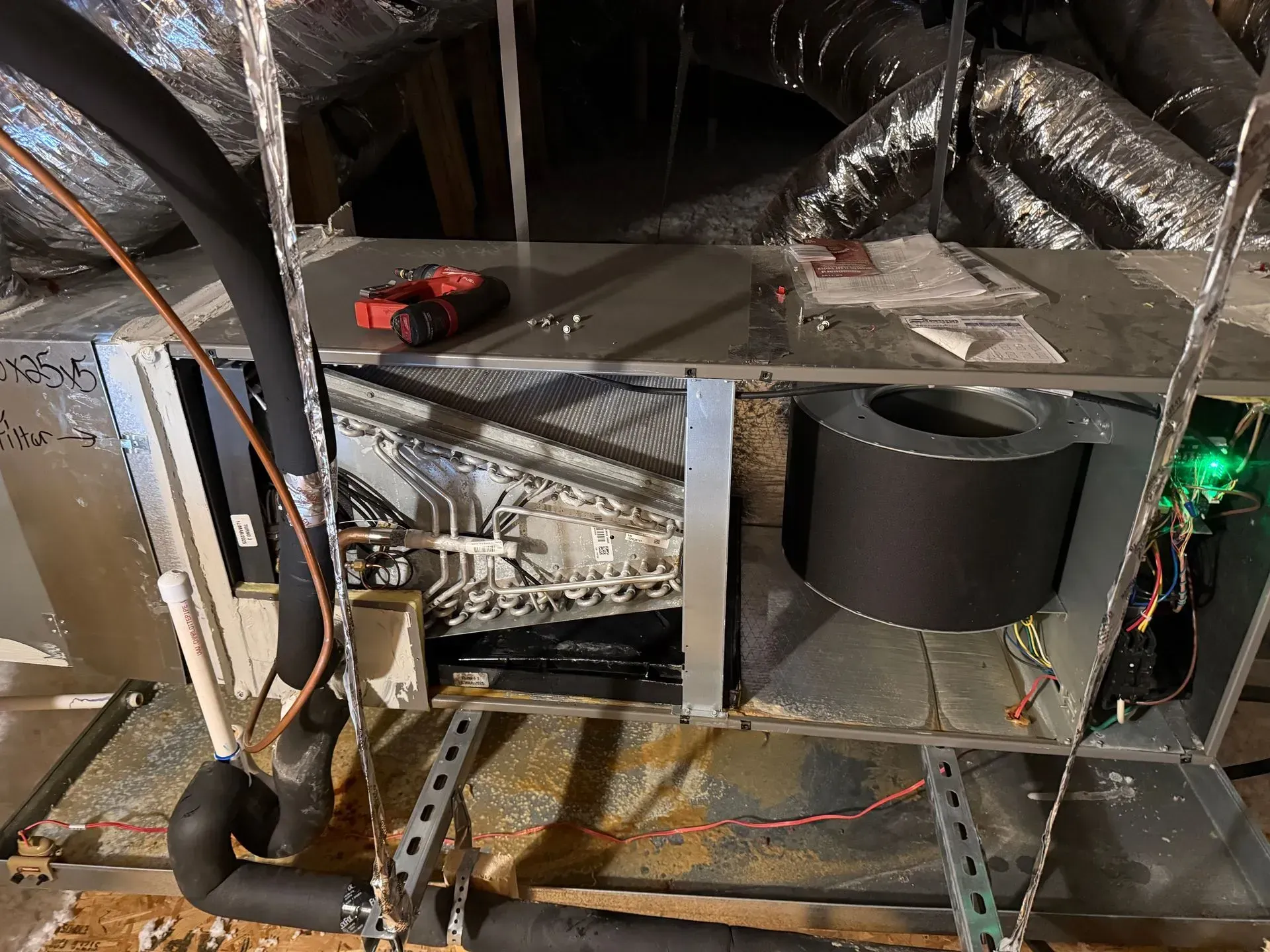 Attic HVAC ducting and metal framing with a black insulated cylinder and a small green light on the right
