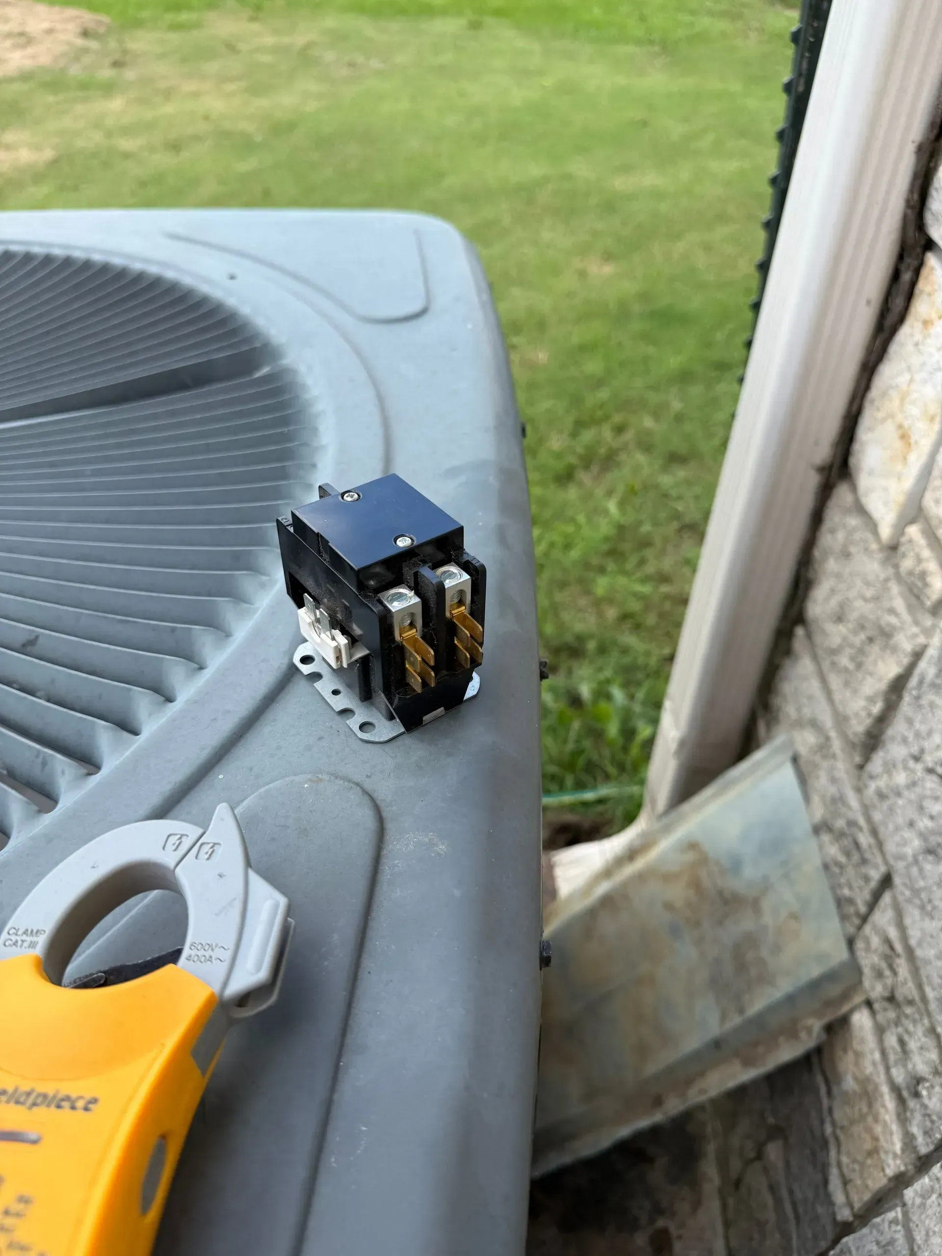 Small black electrical component on an outdoor air conditioner unit near a house wall.