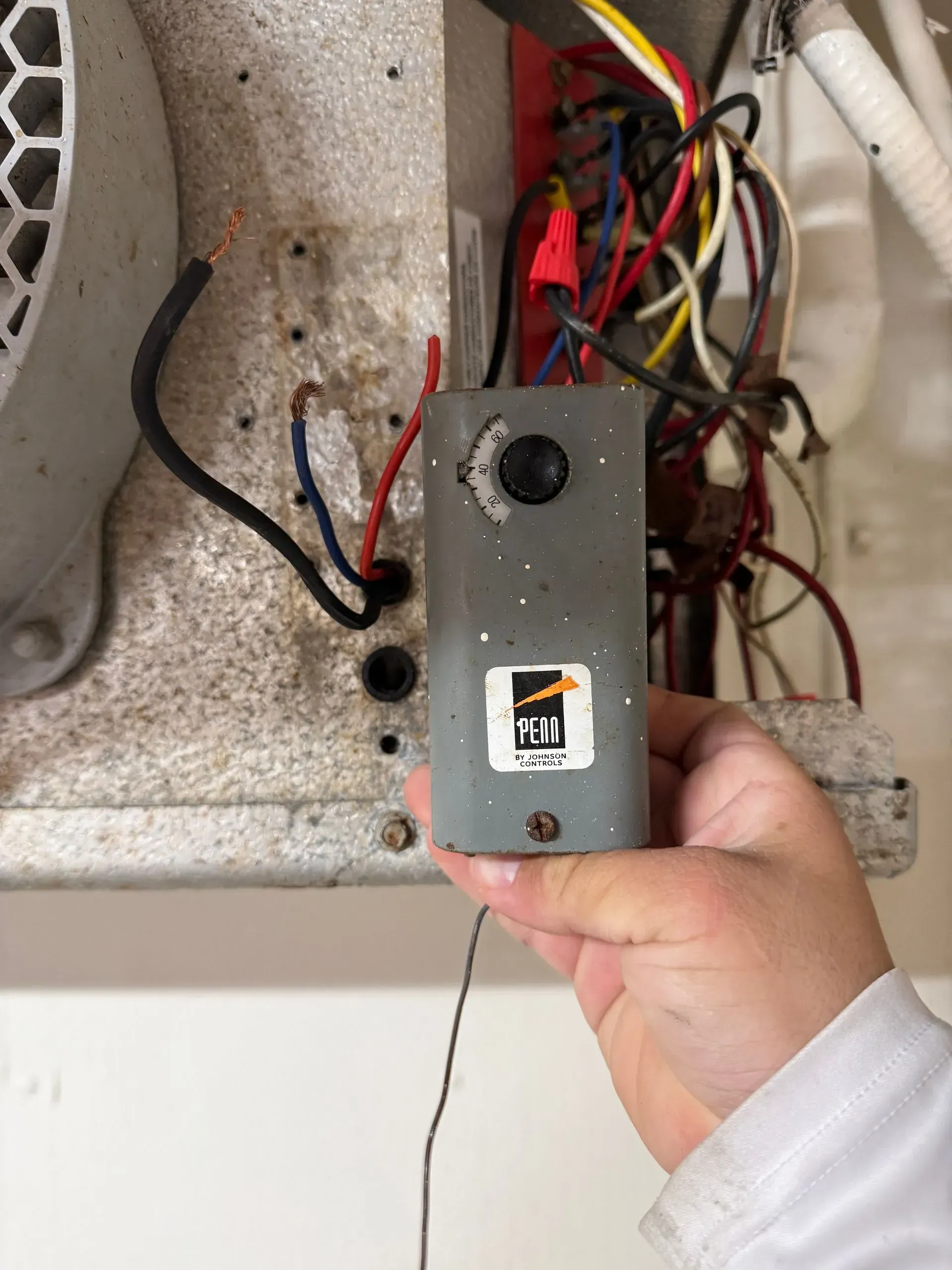 Hand holding a small gray electrical box with wires inside an open wall cavity