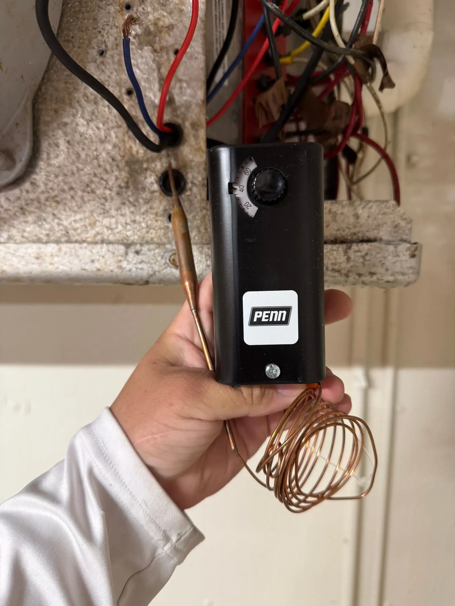 Hand holding a black electrical device with wires under a circuit panel