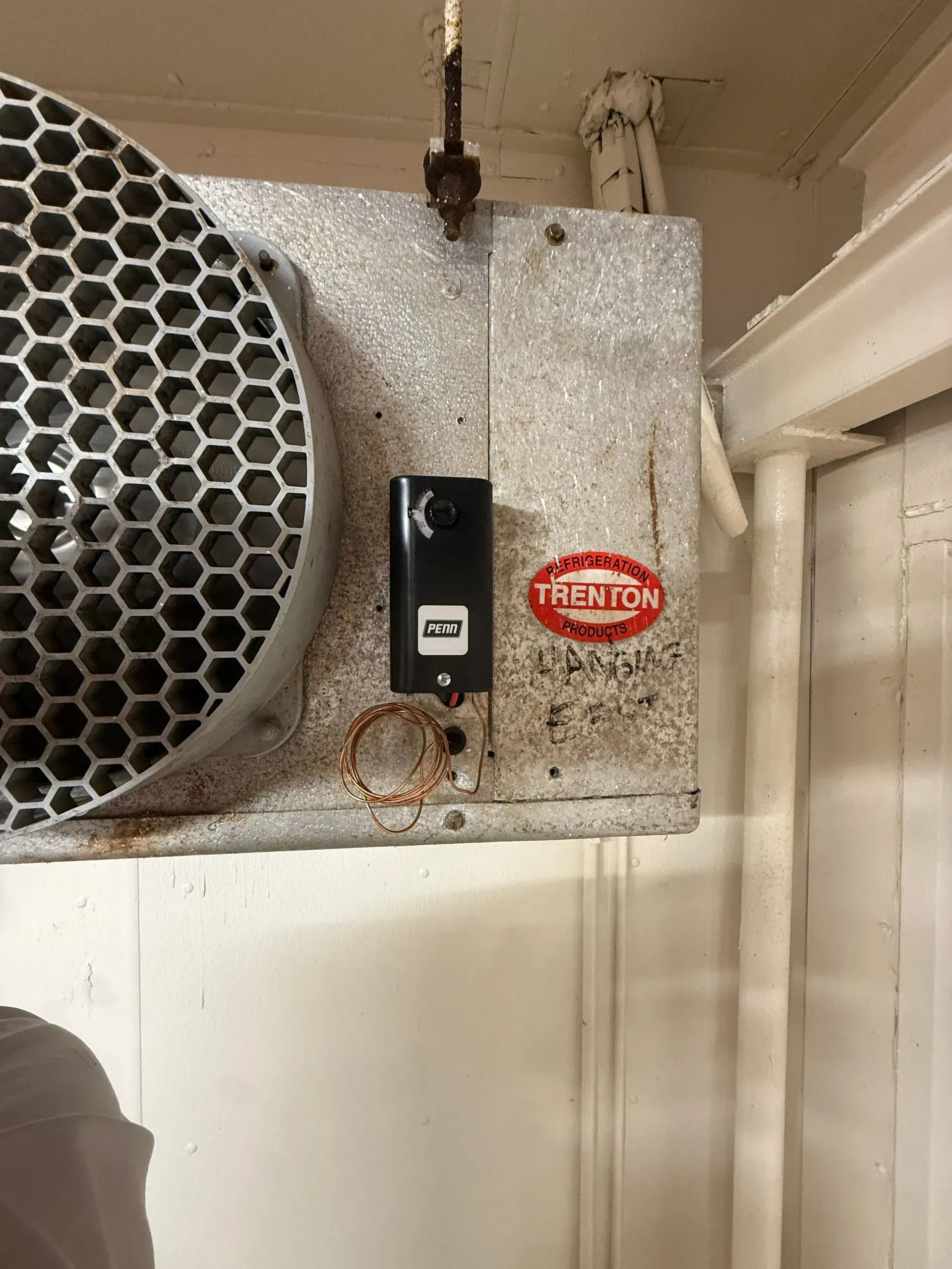 Wall-mounted industrial air vent unit with a honeycomb grille and black control switch on a white wall.