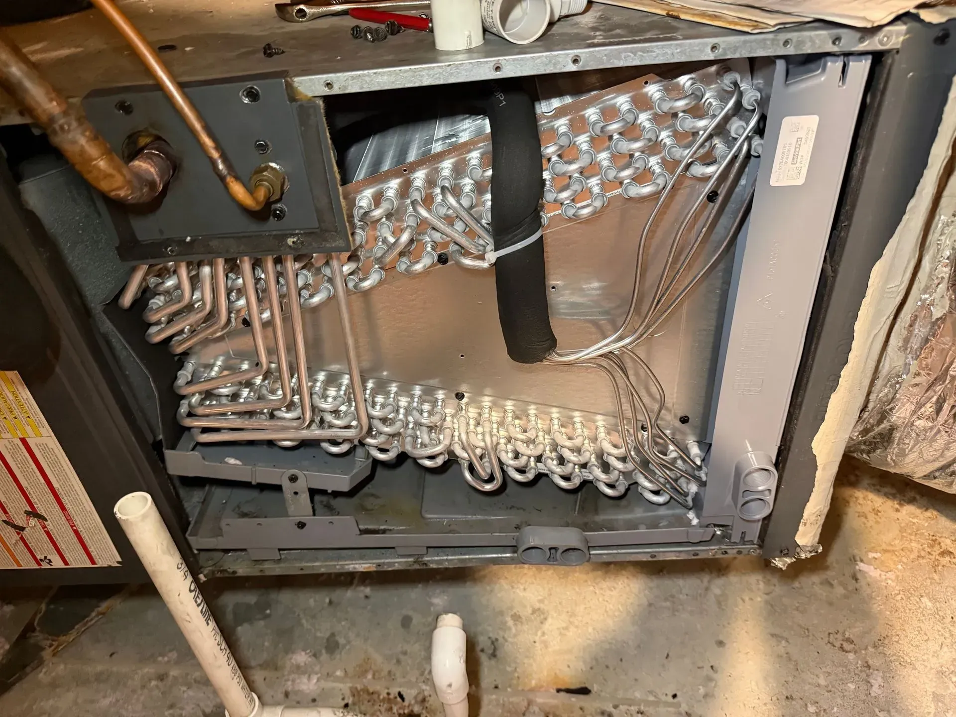 Open HVAC unit with exposed copper tubing, coils, and wiring inside a metal cabinet