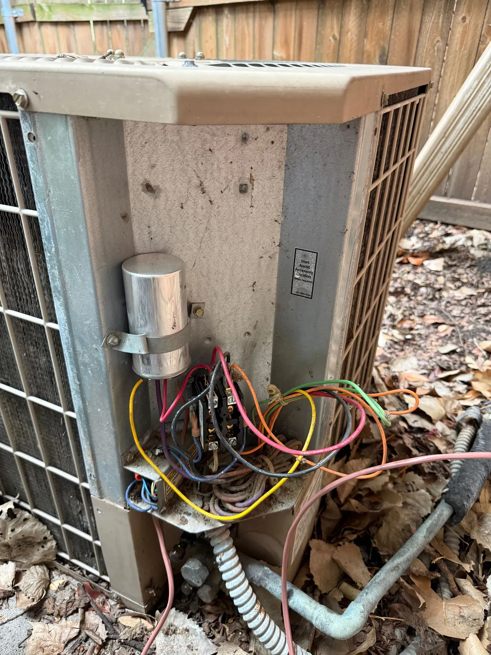 Damaged outdoor HVAC unit with exposed wiring and debris on the ground