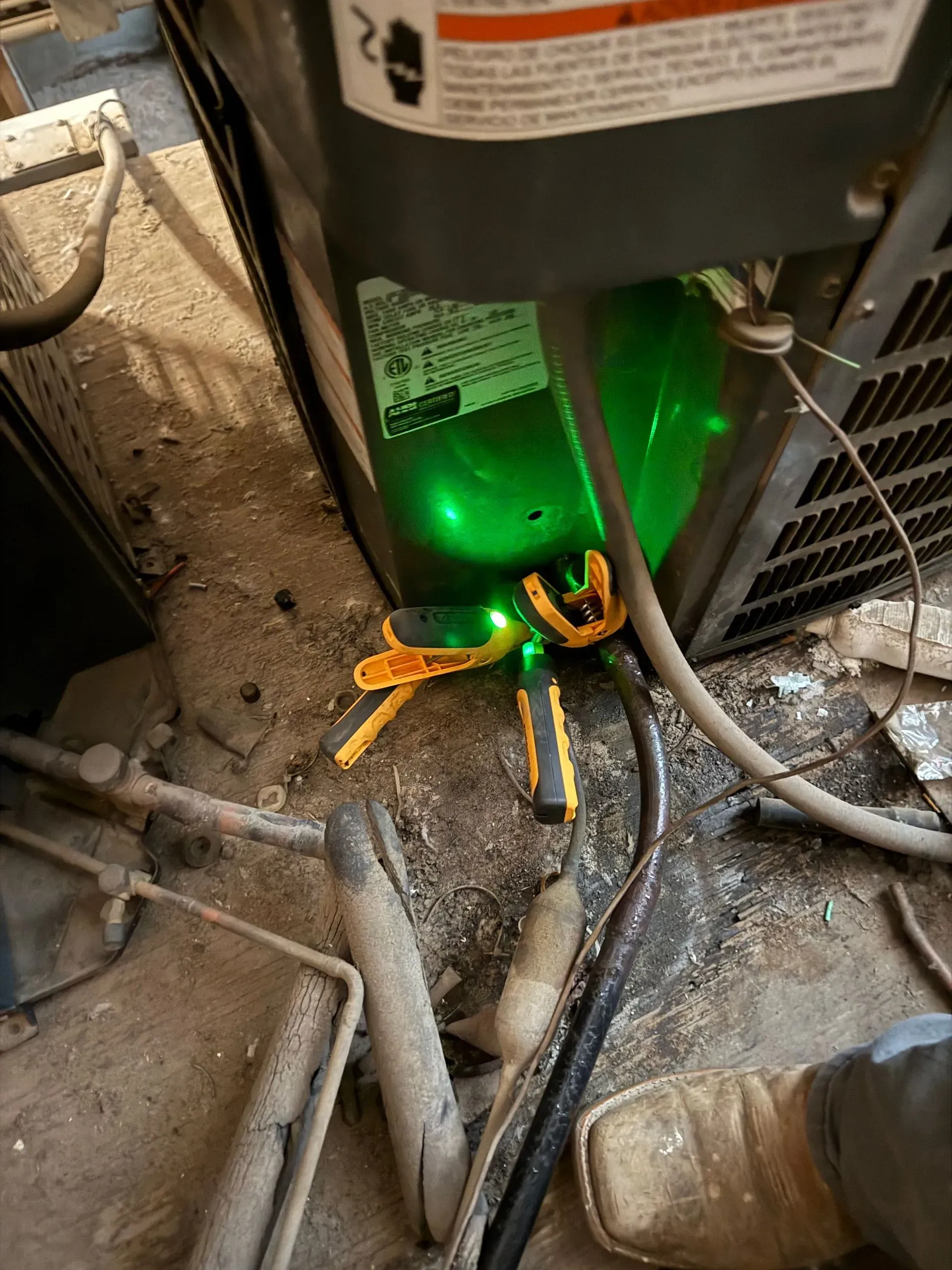 Green-lit electrical panel with tangled orange and black cables on a dusty floor, showing a repair or maintenance scene