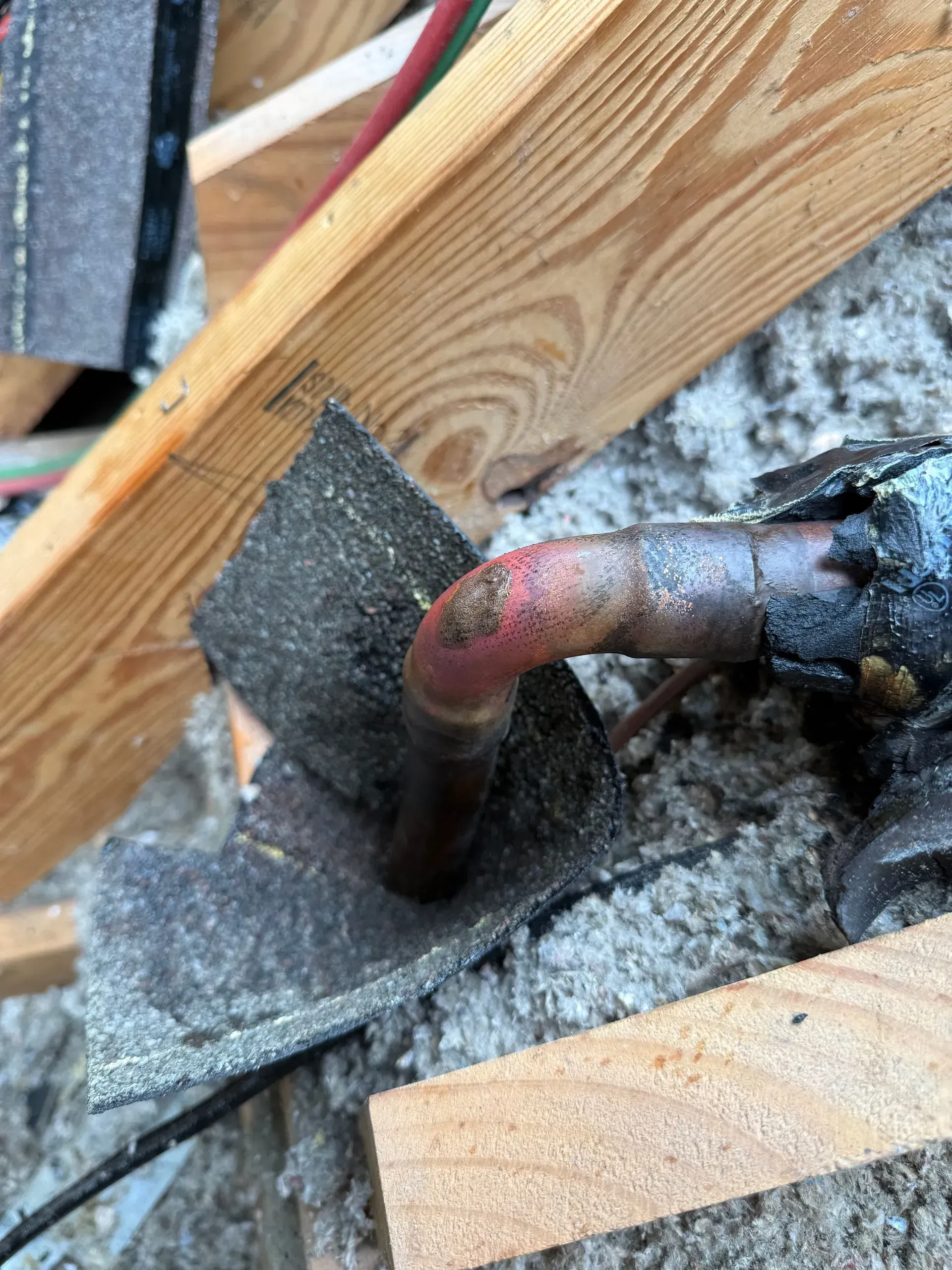 Copper pipe elbow emerging through insulation near wooden framing inside a wall.