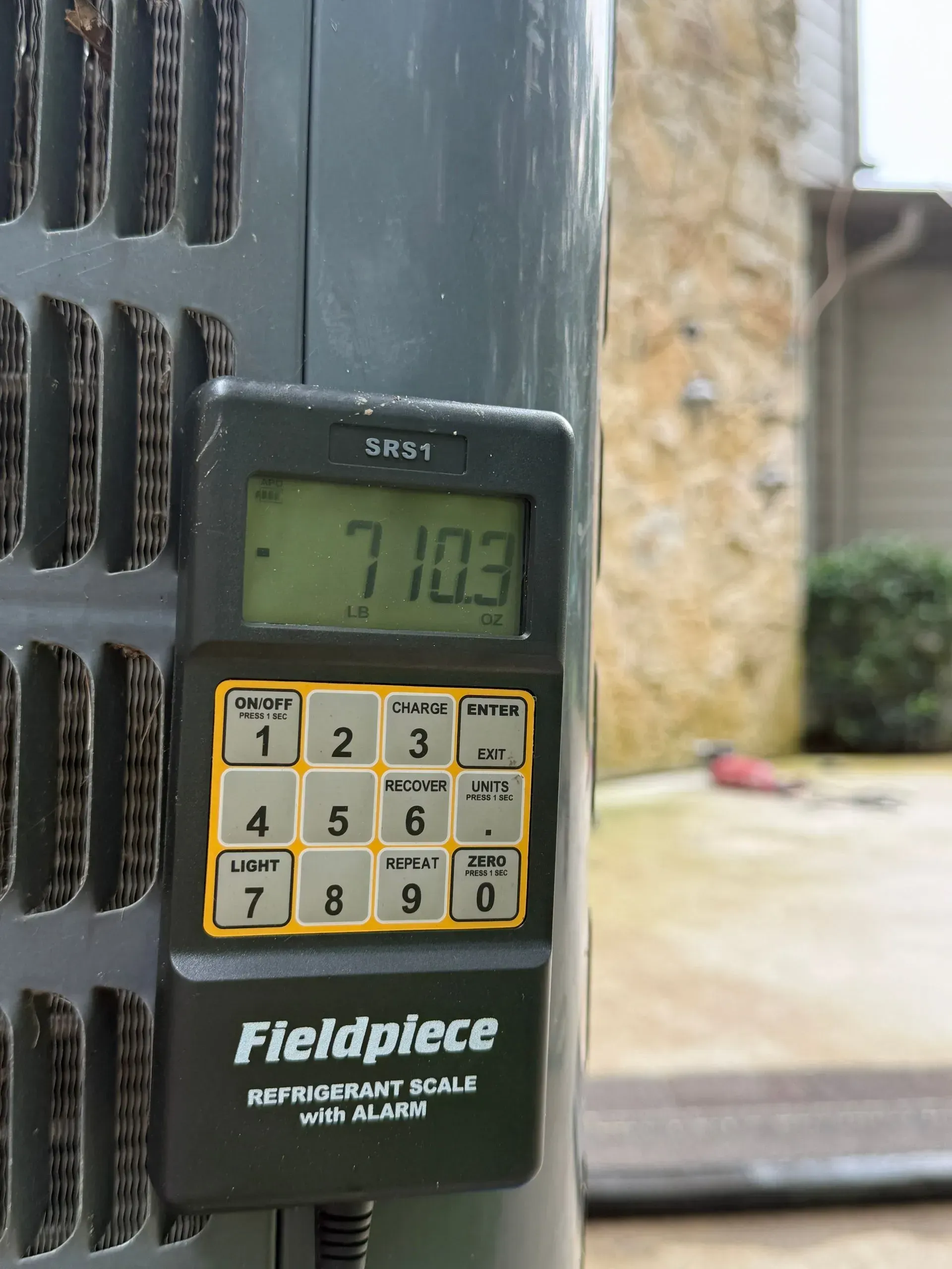 Fieldpiece digital gauge clipped to HVAC unit, displaying 71.03 on screen